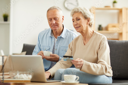 Warm toned portrait of modern senior couple shopping online or paying taxes holding credit card while using laptop at home, copy space