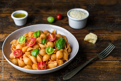 Conchiglie abissine rigate pasta with tomato sauce, cherry tomatoes, and basil against dark wooden background