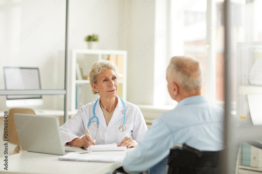 Obraz premium Portrait of female doctor consulting senior man sitting at desk in office, copy space
