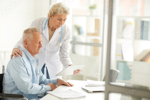 Portrait of female doctor using digital tablet while consulting elderly man, copy space