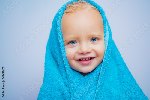 Little baby smiling under a white towel. Small little cute sweet blonde boy bathes in a bath.