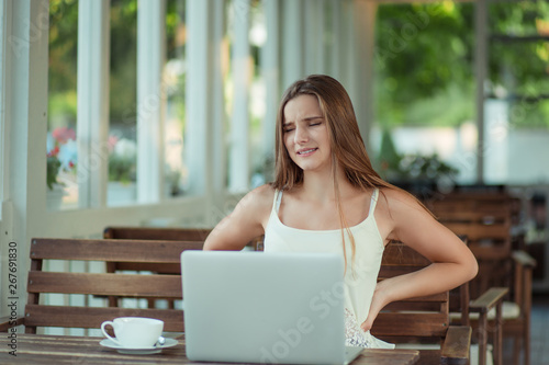 young woman suffering from backache while working in front of the laptop