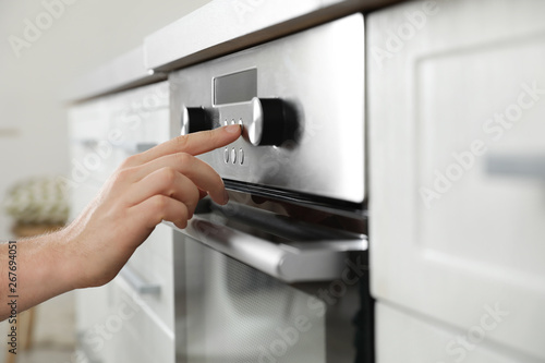 Man regulating cooking mode on oven panel in kitchen, closeup