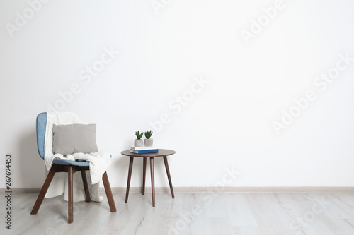 Stylish room interior with chair, pillow and plaid near white wall. Space for text