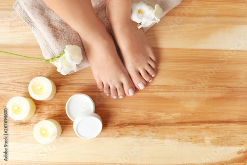 Top view of woman with beautiful feet, candles, flowers and moisturizing cream on wooden floor, space for text. Spa treatment photo