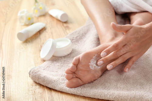 Woman applying foot cream on towel, closeup. Spa treatment
