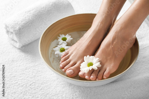 Closeup view of woman soaking her feet in dish with water and flowers on white towel, space for text. Spa treatment