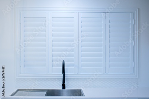 Closed plantation shutters and black kitchen sink mixer tap.