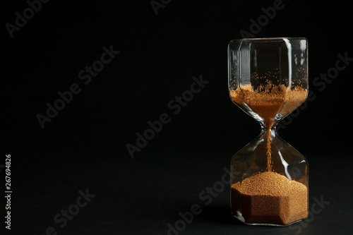 Hourglass with golden sand on black background. Space for text