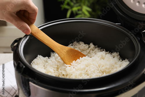 Papier peint Woman taking tasty rice with spoon from cooker in kitchen, closeup