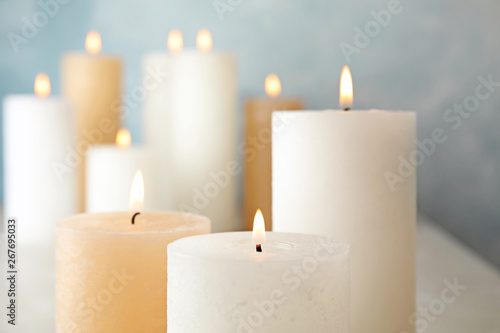 Burning candles on table against color background, closeup