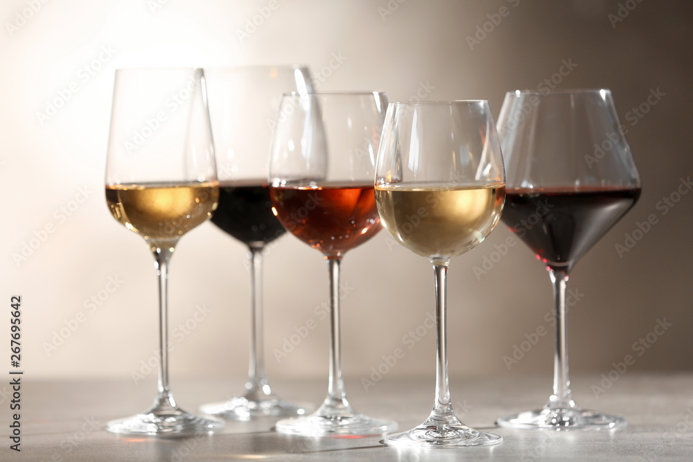 Glasses with different wines on grey table against light background