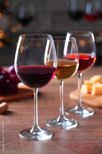 Glasses with different wines and appetizers on wooden table against blurred background