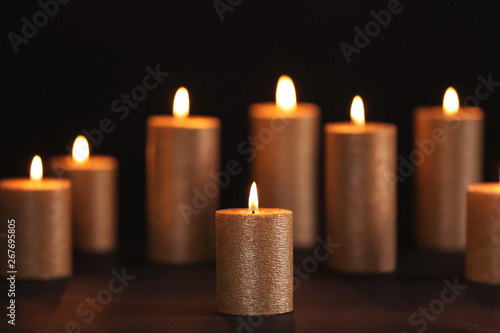 Burning gold candles on table against black background, space for text