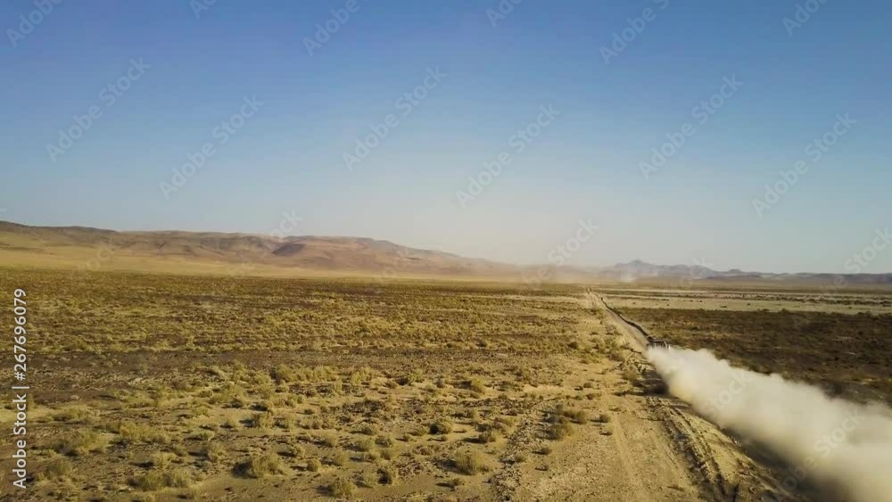Rising aerial shot of an off road vehicle racing away from the camera down a desert track. Rising aerial shot of an off road vehicle racing away from the camera down a desert track.
