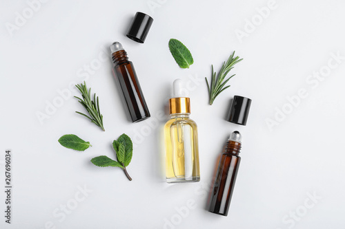 Little bottles of essential oils with different herbs on white background  top view