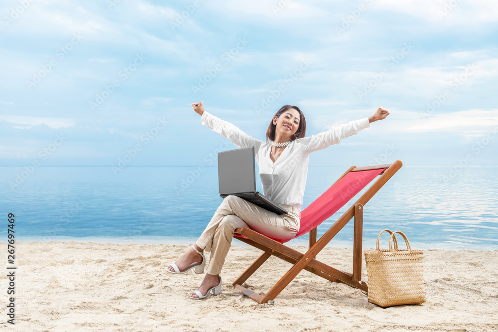 Asian business woman relax when working with laptop sitting in the beach chair on beach