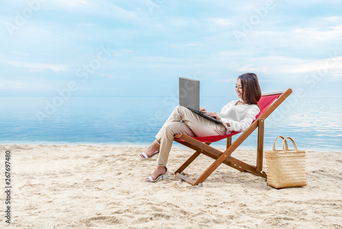 Asian business woman working with laptop sitting in the beach chair on beach