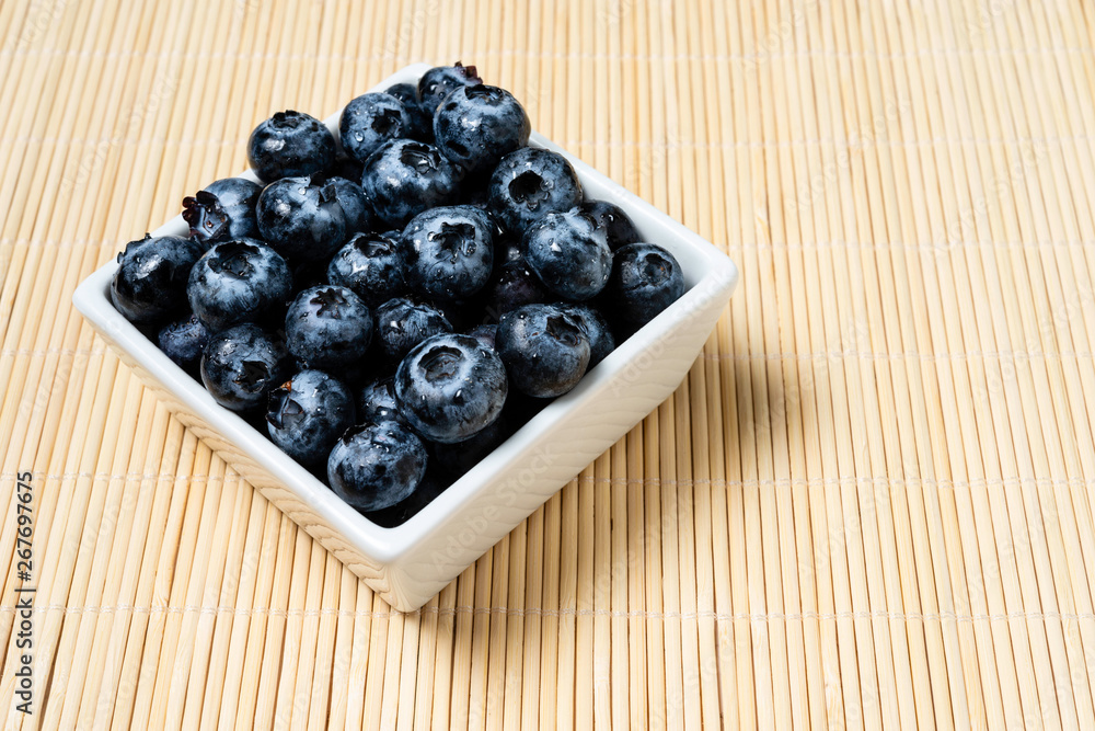 Fresh blueberries inside pot of white ceramic on bamboo background. Fresh blueberries inside pot of white ceramic on bamboo background.