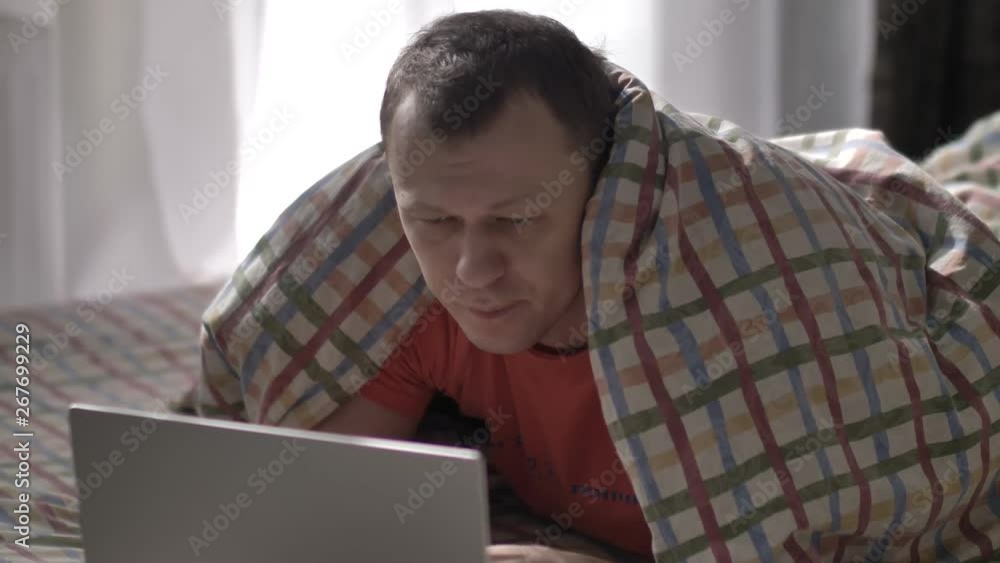 man is lying on a bed and working on a laptop at home man is lying on a bed and working on a laptop at home