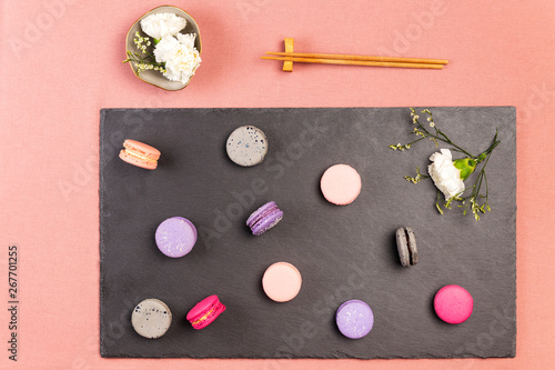 French macarons or macaroons, and incarnation white flower on a slate, with chopsticks and white incarnations flowers in a bowl.