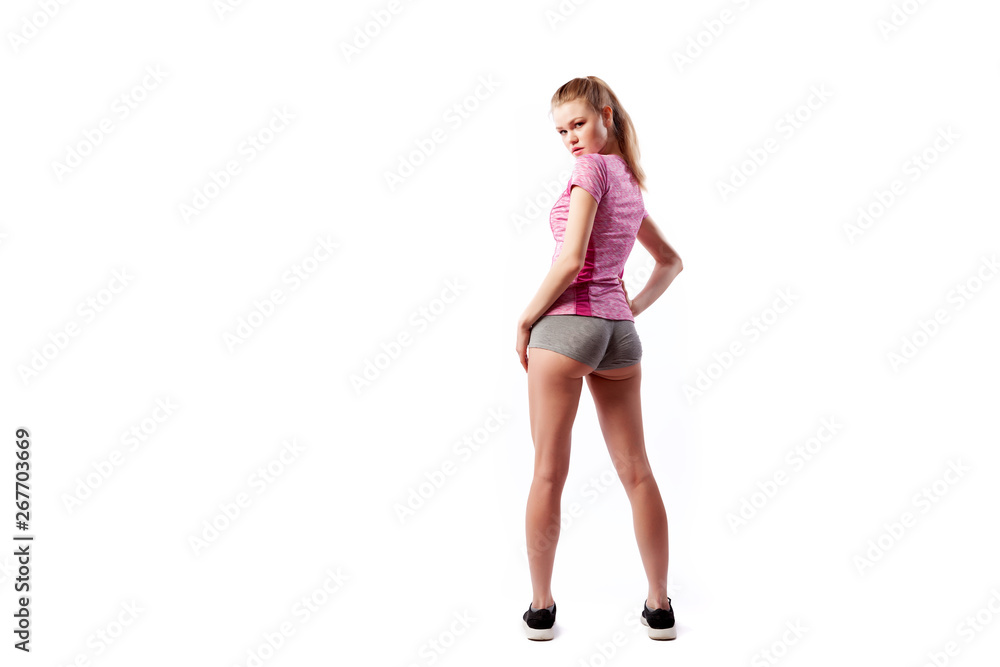 A young slim woman athlete in a sporty pink top and shorts posing and smilling on a white isolated background in studio. Portrait of a beautiful sportswoman A young slim woman athlete in a sporty pink top and shorts posing and smilling on a white isolated background in studio. Portrait of a beautiful sportswoman
