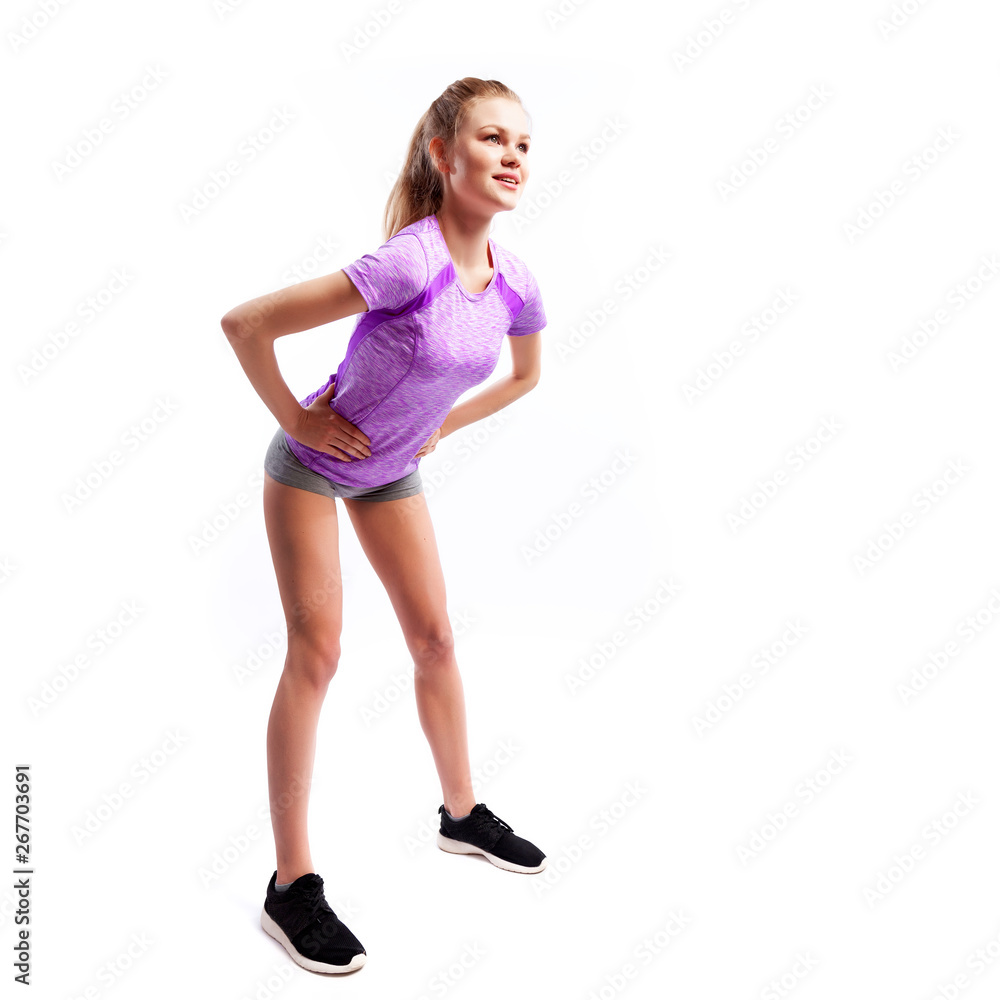 A young woman model in a sporty top and shorts makes bends forward, arms behind waist, legs wide apart on a white isolated background in studio A young woman model in a sporty top and shorts makes bends forward, arms behind waist, legs wide apart on a white isolated background in studio
