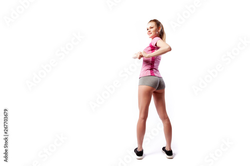 A young slim woman athlete in a sporty pink top and shorts makes turns a side and smilling on a white isolated background in studio, back view. Portrait of a beautiful sportswoman