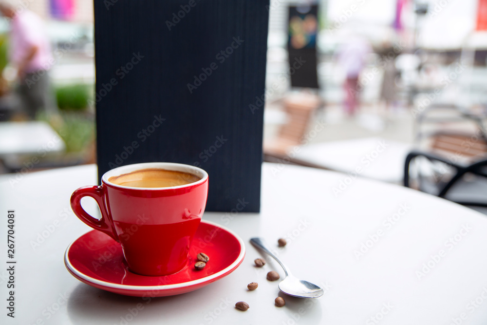Red cappuccino coffee cup mug on a white cafe table interior with menu