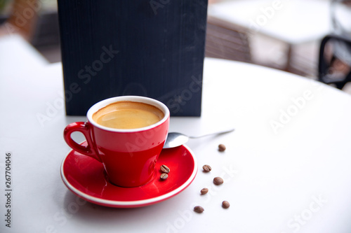 Red cappuccino coffee cup mug on a white cafe table interior with menu