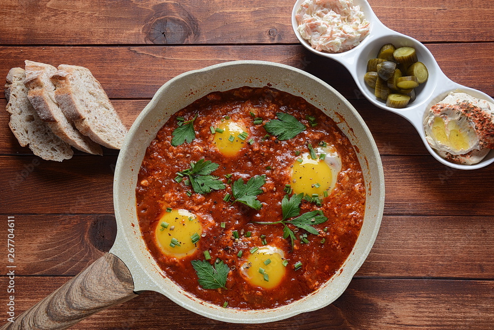 Shakshuka , middle eastern traditional homemade breakfast- fried eggs, onion, bell pepper, tomatoes and parsley in a pan on a wooden background served with hummus Shakshuka , middle eastern traditional homemade breakfast- fried eggs, onion, bell pepper, tomatoes and parsley in a pan on a wooden background served with hummus