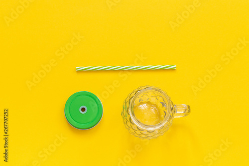 Empty glass jar in form of pineapple with green lid and straw for fruit or vegetable smoothies, cocktails and other beverages on yellow background. Top view Copy space Template.