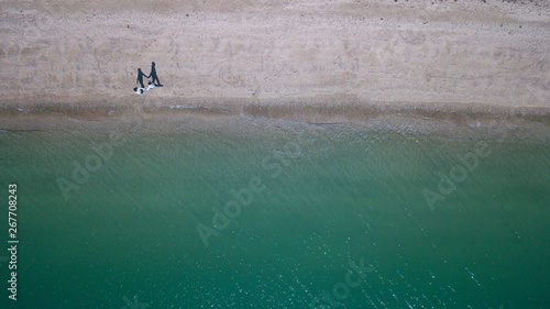 Aerial top down view, couple shadow walks together on beach
