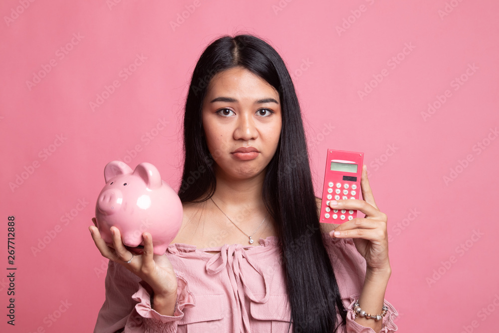 Unhappy Asian woman with calculator and piggy bank. Unhappy Asian woman with calculator and piggy bank.