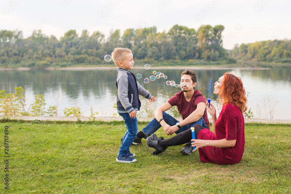 Family and nature concept - Mother, father and their child playing with colorful soap bubbles Family and nature concept - Mother, father and their child playing with colorful soap bubbles