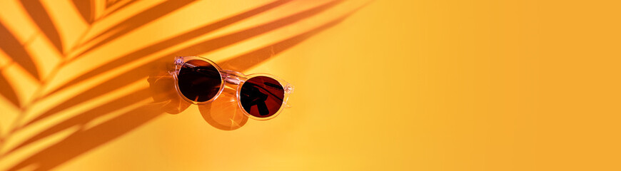 Palm leaf shadow with summer sunglasses on yellow background in sunlight in holiday vacation.banner copy space for display of design