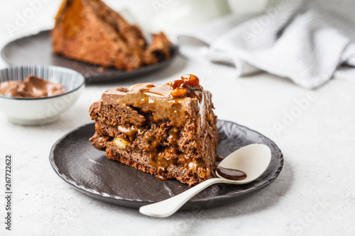 Konstfotografi Piece of homemade snickers cake with chocolate cream and caramel on a black saucer, white background