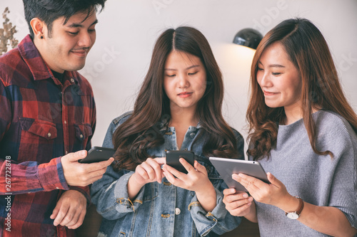 Three young asian people using and looking at mobile phone and tablet pc together