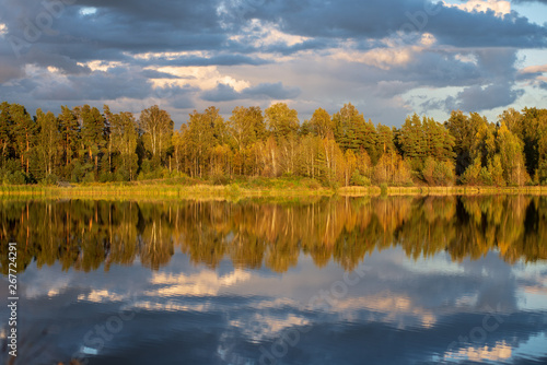 beautiful sunset by the lake with green grass meadow and white clouds in the blue sky