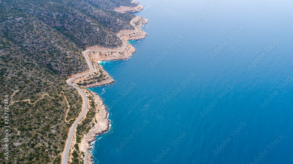 Aerial landscape of coastline and a road seascape. Car drives down the empty asphalt road running along the sunny Mediterranean shoreline of Turkey. Tourist car cruises down the scenic coastal road .