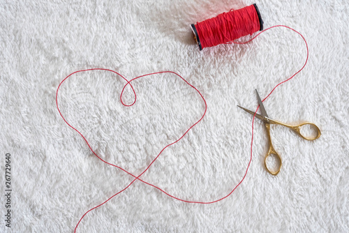 on a white soft background lie a red skein of thread and scissors  a heart is lined from threads © Елена Иващенко