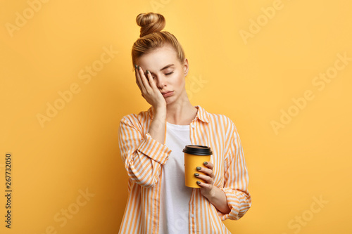 Fototapeta Tired sleepy woman holds a cup of coffee, has sad expression, closes eyes, cannot wake up in the morning and go to work