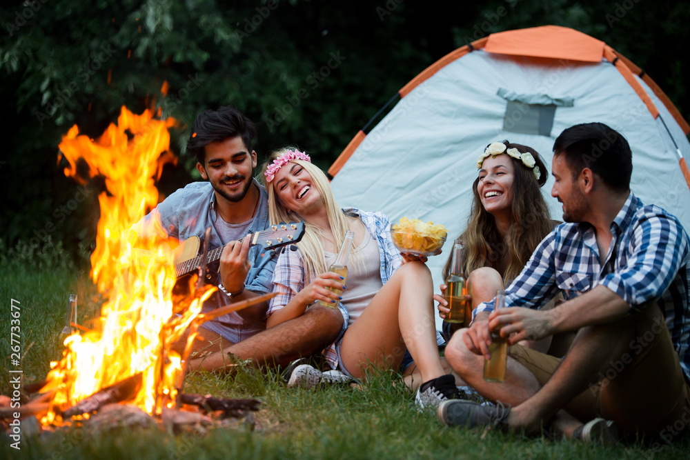 Group of friends camping.They are sitting around camp fire, playing guitar Group of friends camping.They are sitting around camp fire, playing guitar