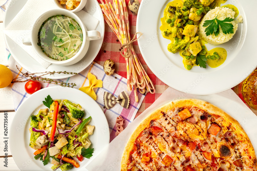 Top view image of italian style business lunch of pizza, soup, steamed vegetables and salad at wooden table background. Top view image of italian style business lunch of pizza, soup, steamed vegetables and salad at wooden table background.