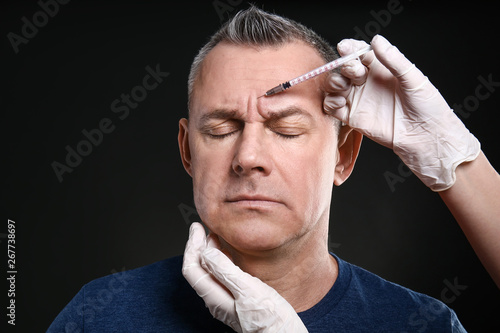 Obraz na plátně Middle-aged man and hands holding syringe for anti-aging injections on dark back