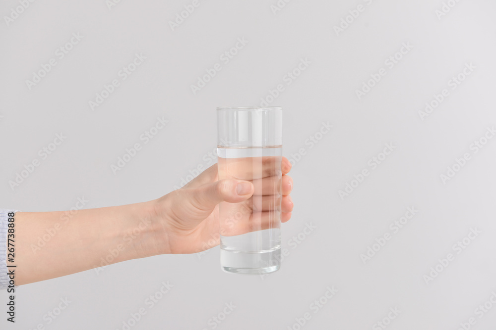 Female hand with glass of fresh water on light background
