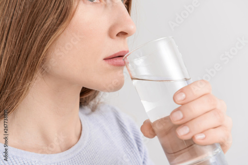 Woman drinking fresh water on light background, closeup