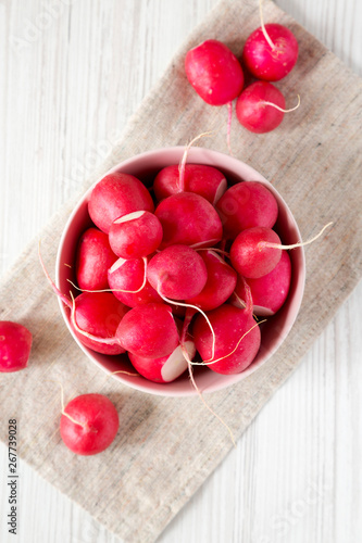 Fresh red radishes in a pink bowl over white wooden background, top view. Flat lay, overhead, from above. Close-up.