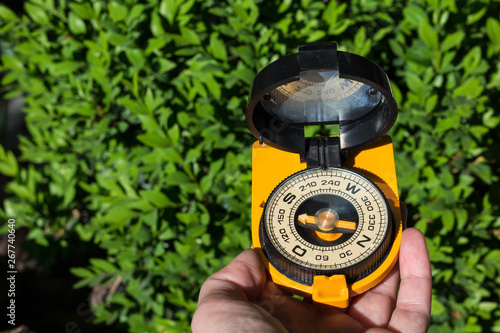 Compass with a big arrow in the hand of a tourist in the forest, green background, space for text