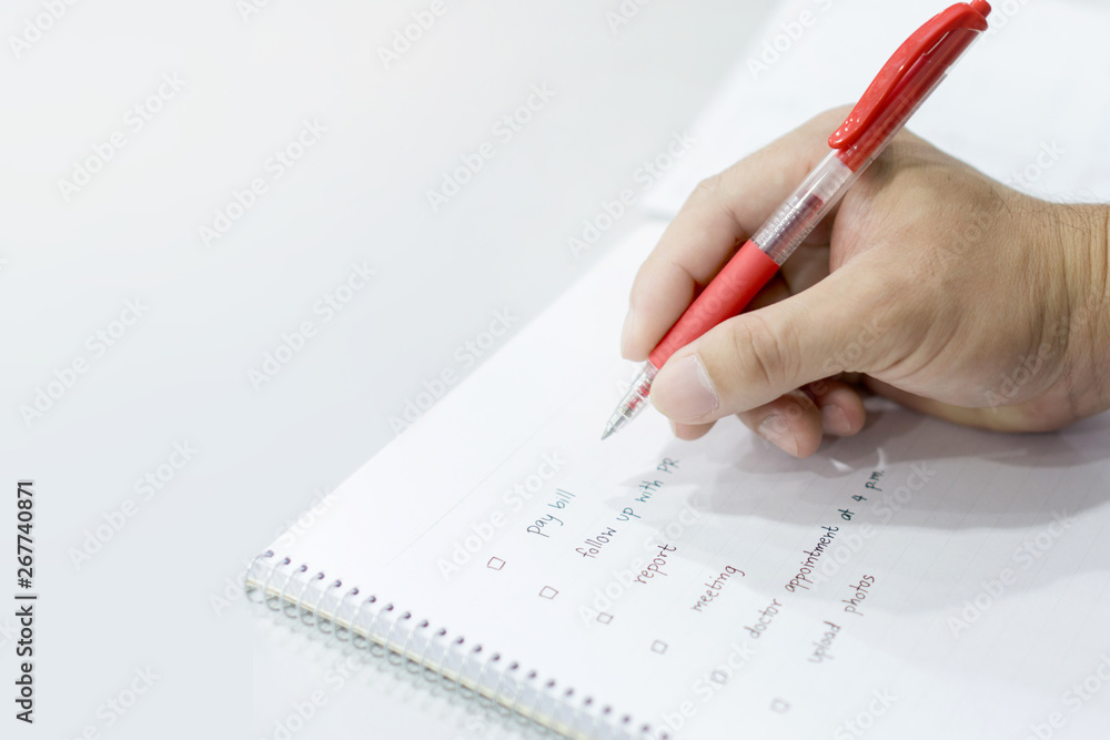 Close up hand holding pen for check list on note scrip Close up hand holding pen for check list on note scrip